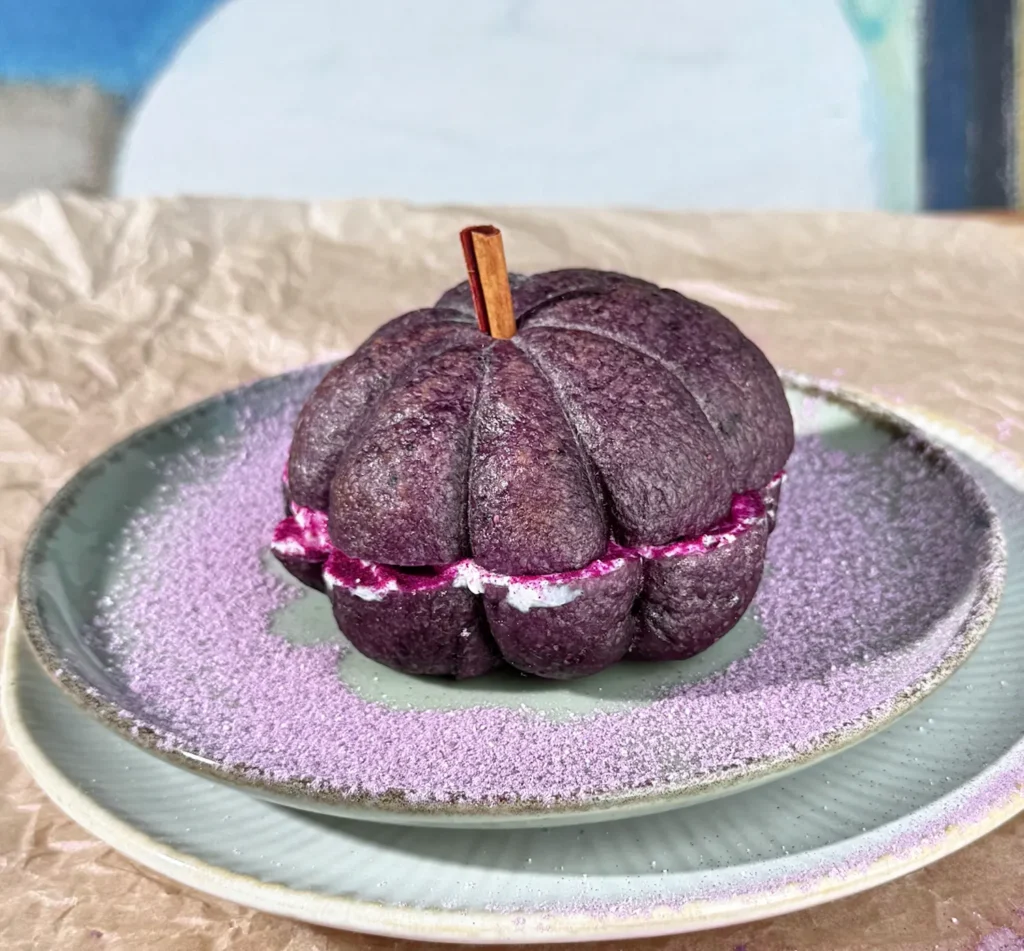 Bagel de arándanos con forma de calabaza, relleno de queso crema de ube, con un palito de canela