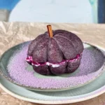 Bagel de arándanos con forma de calabaza, relleno de queso crema de ube, con un palito de canela