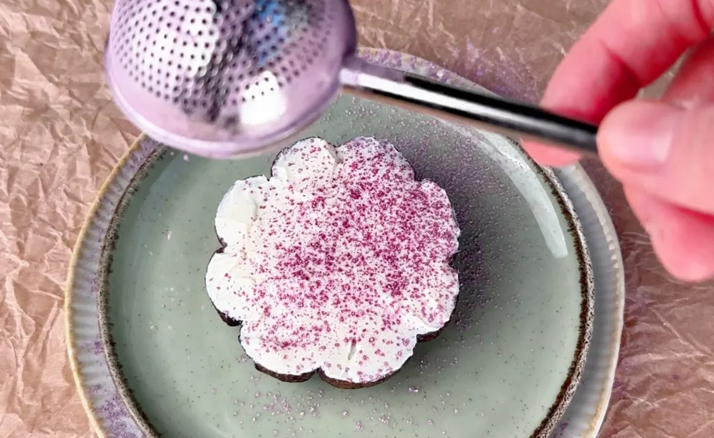 Mitad de un bagel de arándanos con forma de calabaza, untada con queso crema y espolvoreada con polvo de ube morado