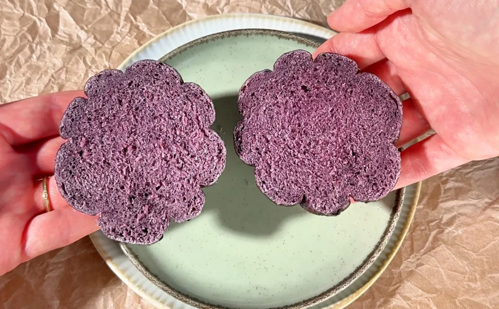 Dos mitades de un bagel de arándanos en las manos, con la miga de un morado intenso