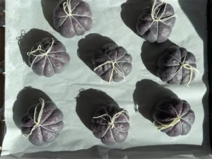 Bagels de arándanos morados atados con hilo de cocina en forma de calabaza, sobre papel de horno antes de hornear