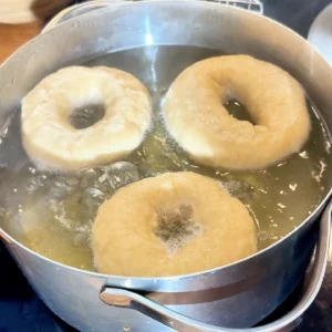 Tres bagels caseros hirviendo en una olla con agua, miel y bicarbonato