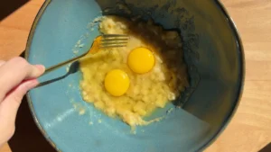 Dos huevos sobre el plátano aplastado, listos para batir con un tenedor