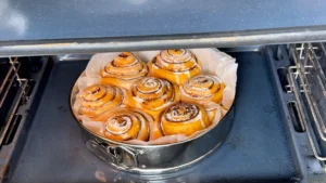 Cinnamon rolls de calabaza horneándose en un molde redondo en la parte media-baja del horno