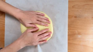 Formando con las manos un disco de masa de brioche sobre papel de horno