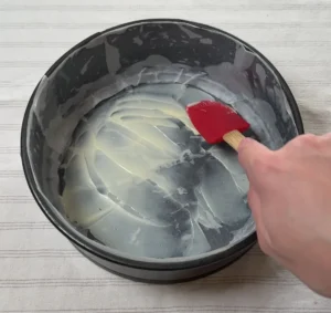 Untando con mantequilla el fondo de un molde desmontable forrado con papel de horno