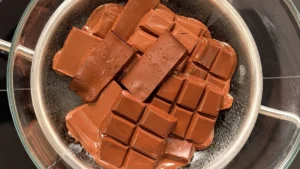 Chocolate fundiéndose al baño María en un bol de cristal sobre un cazo