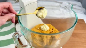 Añadiendo la mantequilla blanda a la masa de calabaza en la amasadora