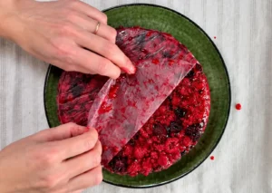 Retirando el papel de horno de la tarta invertida recién desmoldada, con los frutos rojos caramelizados a la vista